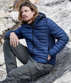 Why Branded Workwear Jackets Matter More Than You Think: A Business Guide to Workwear for the Cold Season 1 A man wearing a blue jacket, and cargo pants. He is sitting on a rock.